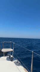Boat passenger films scenic view of sailboat, volcanic coastline