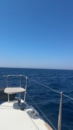 Boat passenger films scenic view of sailboat, volcanic coastline