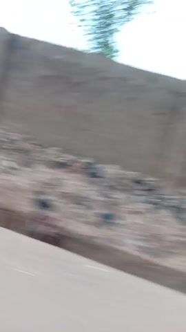 The video appears to be taken from a moving vehicle, possibly a car, as it drives along a street. The focus is on the buildings and structures that line the road. The buildings are a mix of simple designs and colors, including peach and green. The camera movement is fast and somewhat unsteady due to the motion of the vehicle. Overall, the scene is a quick glimpse of a residential or urban area as the vehicle passes through it.