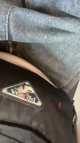 The video shows a person's legs and feet while they are sitting down. They are wearing blue jeans with orange stitching and white sneakers with red and black writing on them. The person is wearing a black fanny pack with a Prada logo on the front. The background is white.