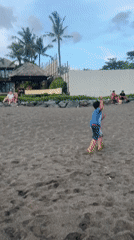 Beachgoers spotted on dark sand in Mengwi, Indonesia