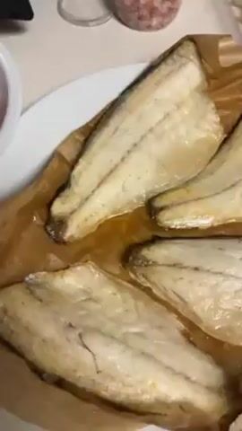 The video shows a close-up of a plate of baked fish on parchment paper, a bowl of halved cherry tomatoes, and a pot of cooked spiral pasta on a stovetop.