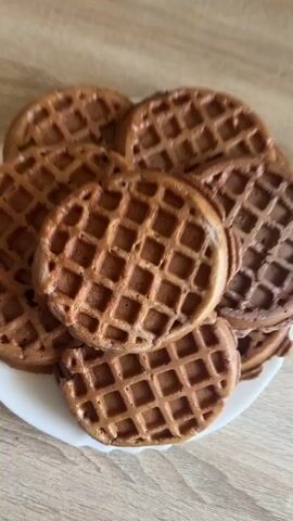The video shows a plate of waffles. The waffles are round and have a grid pattern. They appear to be chocolate flavored. The plate is white and is sitting on a wooden surface. The video is shot from a top-down perspective.
