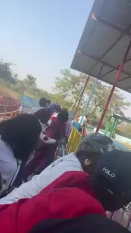 The video shows people at a water park waiting in line for a ride.  The ride appears to involve alligator-shaped boats that float in a narrow channel. A man wearing a red shirt marked "Operator" is seen moving one of the boats. The water park includes blue and light blue slides and other water features. The weather appears sunny.