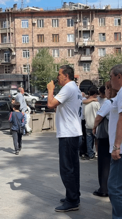 Group gathers on Yerevan sidewalk, man speaks into microphone