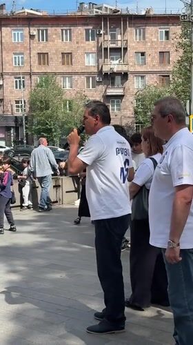 Group gathers on Yerevan sidewalk, man speaks into microphone
