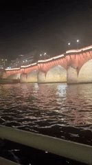 Parisian bridge lit red over a calm river at night