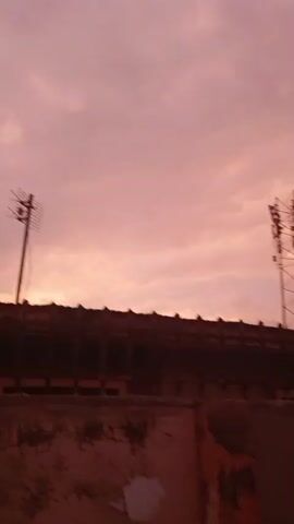 The video captures a sunset in Nigeria. The sky is a vibrant pink and orange, with clouds swirling across it. In the foreground, there's a silhouette of a building with a transmission tower. The camera is moving, creating a slightly blurry effect in some frames. The overall atmosphere is serene and beautiful, highlighting the natural splendor of the Nigerian landscape at dusk.