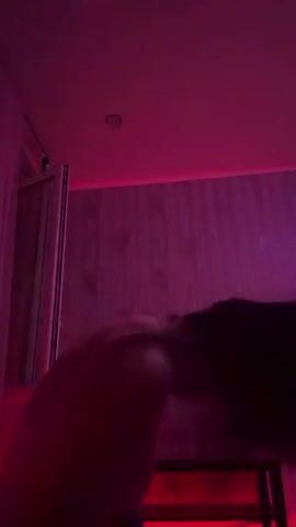 This is a short, blurry video clip, likely taken indoors in a room with colored lighting. The subject appears to be a person, possibly a woman, dancing or moving dynamically. The lighting shifts between green, pink, and purple hues, creating a vibrant, possibly club-like or party atmosphere. The person is wearing a bright pink top. The background features patterned wallpaper and what looks like a closet or door frame. The overall impression is one of energetic movement and a visually stimulating environment. There is no discernible text in the video. Given the Ufa, Russia location context, it is possible this was filmed in a residential setting, a club, or a venue. The time of day is not specified but the lighting suggests it is likely evening or night.