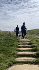 Two hikers with dog climb wooden stairs in Étretat