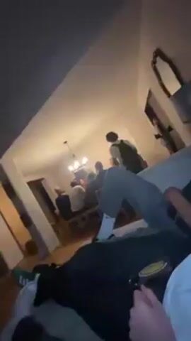 Here is a forensic description of the video:

The video is taken indoors, likely in a living room. Several people are present, some sitting on a light-colored sofa. One young man is prominently featured, leaning back on the sofa with a toothpick in his mouth. He has curly hair and appears flushed. The camera focuses closely on his face as he speaks, though the audio is unclear. Other individuals are visible in the background, though their actions are less defined. The lighting is somewhat dim, with a visible light fixture in the background.