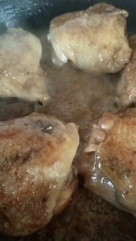 This media file shows a close-up, overhead view of several pieces of seasoned chicken thighs being pan-fried in a dark pan. The chicken pieces are golden brown with some darker seared areas, and they are immersed in bubbling oil or rendered fat. The lighting is artificial, suggesting an indoor setting, likely a kitchen. The focus is on the food, highlighting the cooking process. There is no visible text or information about the time of day, weather, or specific location beyond the general context of a home kitchen. The activity is the cooking of chicken.