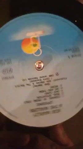The video shows a close-up of a blue-labeled vinyl record spinning on a record player. A silver spindle is at the center of the record. The record label features the artist "BOB MARLEY & THE WAILERS" and the album title "UPRISING". Below this, the tracklist for Side 1 is visible, including "COMING IN FROM THE COLD," "REAL SITUATION," "BAD CARD," "WE AND THEM," and "WORK."

Further text on the label indicates "PRODUCERS: Bob Marley & The Wailers" and "Chris Blackwell," along with "℗ 1980 Island Records Ltd." Other details include "STEREO," the catalog number "ILPS 9646," "SIDE 1," and "MADE IN UK." The distinctive Island Records logo, featuring a palm tree, sun, and a person, is prominently displayed on the right side of the label. A hand is briefly visible in the bottom right corner of the frame. The setting appears to be indoors, potentially in Lyon, France, as per the provided context.