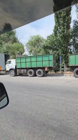The video shows several large trucks parked along a road. The first truck is a grey semi-trailer with a tarp. The second truck has an advertisement for "HOTEL ENERGETIC". The third truck is covered in a green tarp. The fourth truck has an advertisement for "swisspor saving energy". The last truck is a grey semi-trailer with the logo "SCHMITZ CARGOBULL". The video appears to be taken from inside a vehicle, as a side mirror is visible in the lower left corner. The environment consists of trees and a cloudy sky.