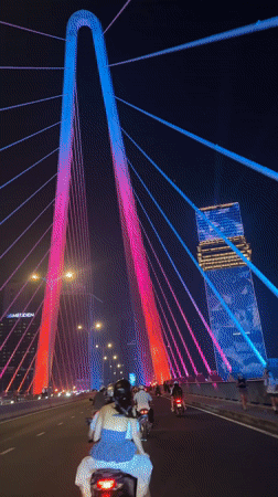 Motorbike passenger crosses colorful lit bridge in Ho Chi Minh City