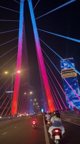 Motorbike passenger crosses colorful lit bridge in Ho Chi Minh City