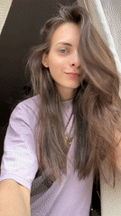 Woman adjusts hair while standing at window in Krasnoyarsk