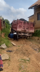 Red dump truck stuck in mud, crew working to recover it