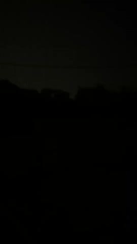 A grainy, dark video shows a silhouette of trees and structures against a dimly lit sky. A faint horizontal line, possibly a power line, is visible in the upper portion of the frame. The overall impression is of a nighttime scene, possibly with some ambient light or distant lightning.