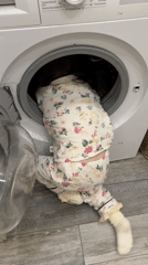 Child climbs into washing machine wearing floral pajamas