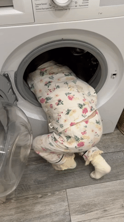 Child climbs into washing machine wearing floral pajamas