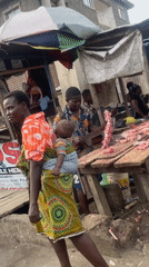Woman with baby walks past butcher stall in Lagos market