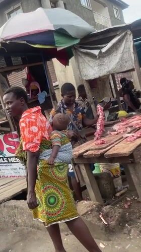 Woman with baby walks past butcher stall in Lagos market