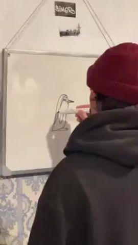 A person wearing a black hooded jacket and a maroon beanie is drawing on a white board. The person is facing the whiteboard and is using a red marker to add details to a drawing of a penguin. The whiteboard is hanging on a wall with patterned wallpaper. There are stickers on the wall above the whiteboard.