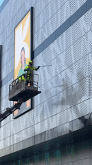 Worker pressure-washes building facade from cherry picker in Moscow