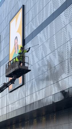 Worker pressure-washes building facade from cherry picker in Moscow