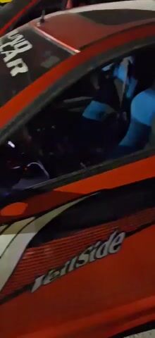The video pans across the engine bay of a red car. The hood is open, revealing a complex arrangement of engine components, including various pipes, wires, and what appears to be a battery. The engine is highly customized with visible carbon fiber accents on some parts. The car has a racing-inspired decal on the windshield that reads "SOUNDSTREAM". The scene appears to be outdoors at night, with artificial lighting illuminating the engine bay. There are no people or interactions visible in the video.