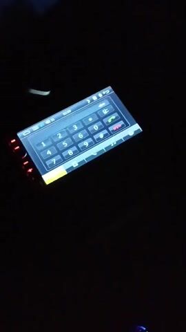 The video shows a close-up of a car's dashboard screen at night. The screen displays a numerical keypad, resembling a phone dialer interface, with green illuminated buttons along the left side of the screen. The screen is tilted slightly upwards and to the right. The background is dark, suggesting the car's interior is dimly lit or the video is being recorded in low light conditions.