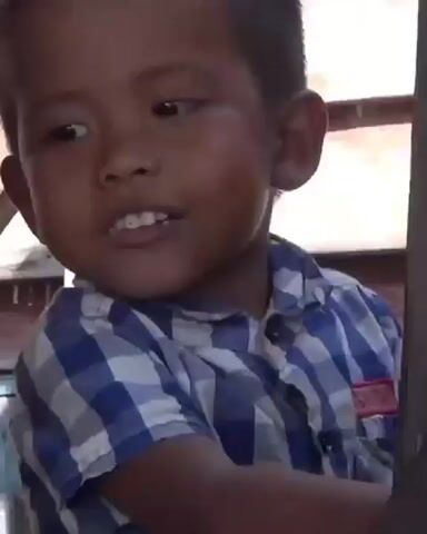 A young boy wearing a blue and white plaid shirt is shown. He is looking to his left with his mouth open. He then turns to his right and begins to eat a piece of bread.