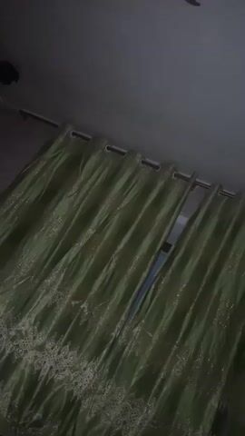 A video shows a pair of open green curtains with gold embroidery on the bottom. The curtains are hanging from a rod, and there is a gap in the middle where they are parted. The background is dark, with a sliver of light visible through the gap in the curtains. The video is short and does not show any people or other objects.