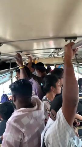 The video shows a crowded bus interior. Many passengers are standing, holding onto overhead handrails for support. The bus appears to be in motion. People are dressed in casual clothing. The light is muted inside the bus. The environment appears to be urban.