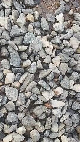 A close-up aerial view of a surface covered in small, gray and white stones, with patches of dirt visible between them. The stones are of various shapes and sizes, and the camera appears to be moving slowly downwards. There are no people or animals visible in the video.