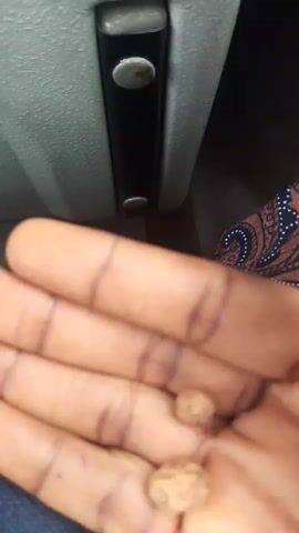 The video shows a close-up view of a person's hand holding two small, round, light brown objects. The hand is dark-skinned and appears to be in a resting position, with the fingers slightly curled. The objects are roughly spherical and have a textured surface, resembling seeds or small stones. The background is out of focus but appears to be indoors, possibly within a vehicle, as suggested by the presence of a grey panel with buttons or levers. The lighting suggests it is daytime. There is no discernible text within the video. The focus of the video is on the two objects in the palm of the hand.