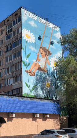 Mural of smiling girl on swing observed on apartment building