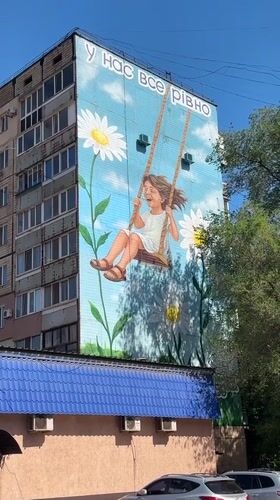 Mural of smiling girl on swing observed on apartment building