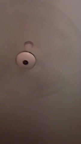 The video shows a ceiling fan. The fan is white with a black center. The blades are not visible. The camera slowly zooms in closer to the fan. The ceiling is also white.