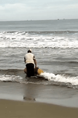 Indonesian fisherman works beach with baskets, nets near traditional boat