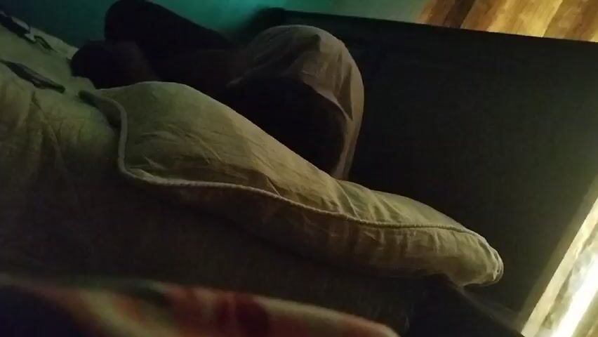 Here is a description of the video:

The video shows a bedroom. A bed is visible in the foreground, partially covered with a sheet and pillow. The background features a dark headboard and a window with brown curtains. A wall painted in a blue-green hue can be seen to the side of the window. As the camera angle adjusts, the top of the curtains is revealed, showcasing the curtain rod and a white air conditioning unit on the ceiling.