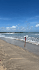 Person with umbrella walks Kuta beach at dawn