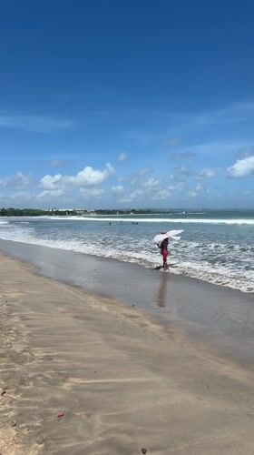 Person with umbrella walks Kuta beach at dawn
