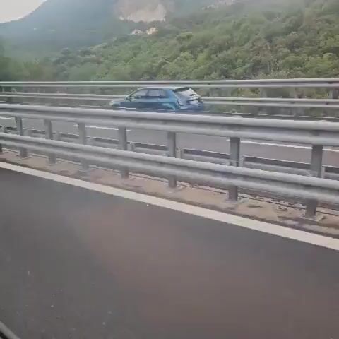 A red Ferrari is seen driving on a highway. The car passes by other vehicles and goes through a tunnel. The video appears to be filmed from another car.