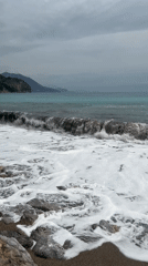 Waves crash on rocky Montenegro beach under cloudy skies