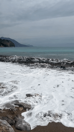 Waves crash on rocky Montenegro beach under cloudy skies