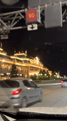 Car approaches ornate illuminated building in Estosadok at night