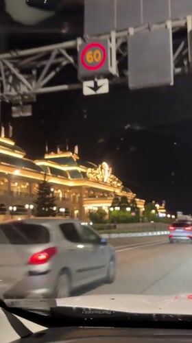 Car approaches ornate illuminated building in Estosadok at night