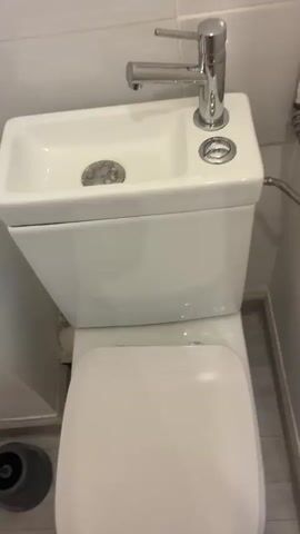 The video shows a white toilet with a sink built on top of the tank. A hand turns on the faucet of the sink and water starts to flow. The person turns off the faucet and presses the button to flush the toilet.